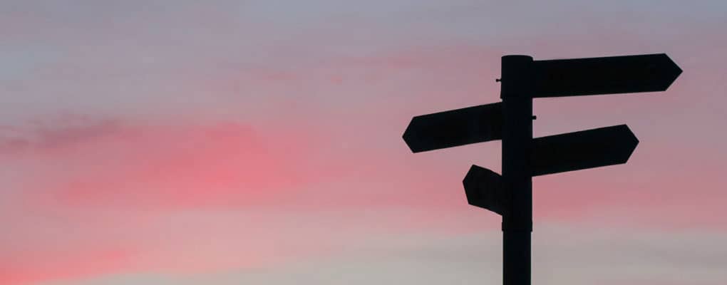 Silhouette of signpost against sunset sky